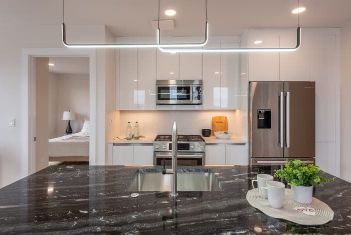 Kitchen with a dark marbled island, built-in appliances, and a view of an adjacent room.