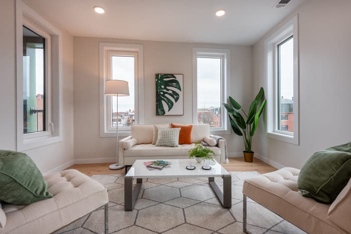 Cozy living room with a white sofa, leafy wall art, and a view of the city through windows.