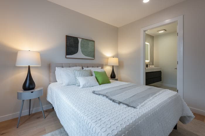 Neat bedroom with a comfortable bed, elegant lamps, abstract wall art, and a view of an ensuite bathroom.